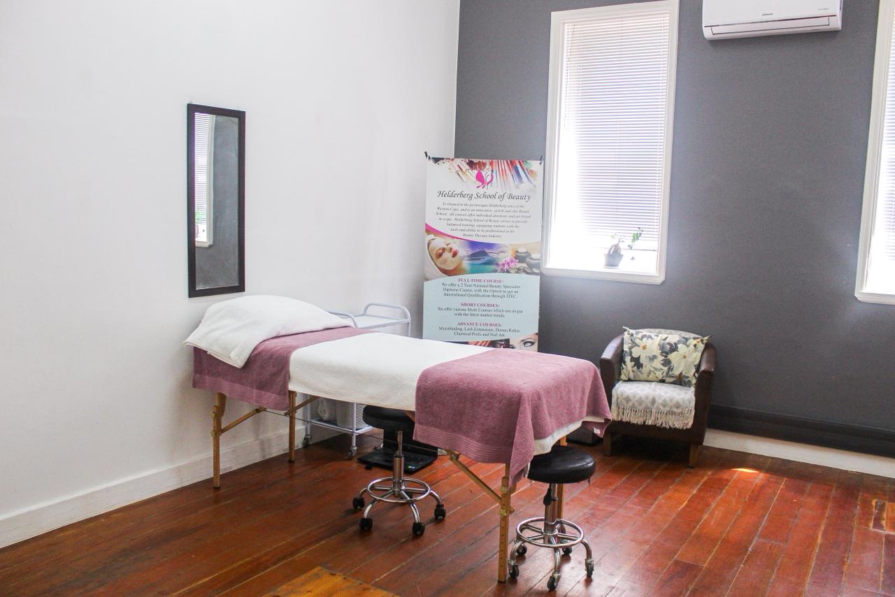 Treatment room with massage bed and Helderberg School of Beauty banner