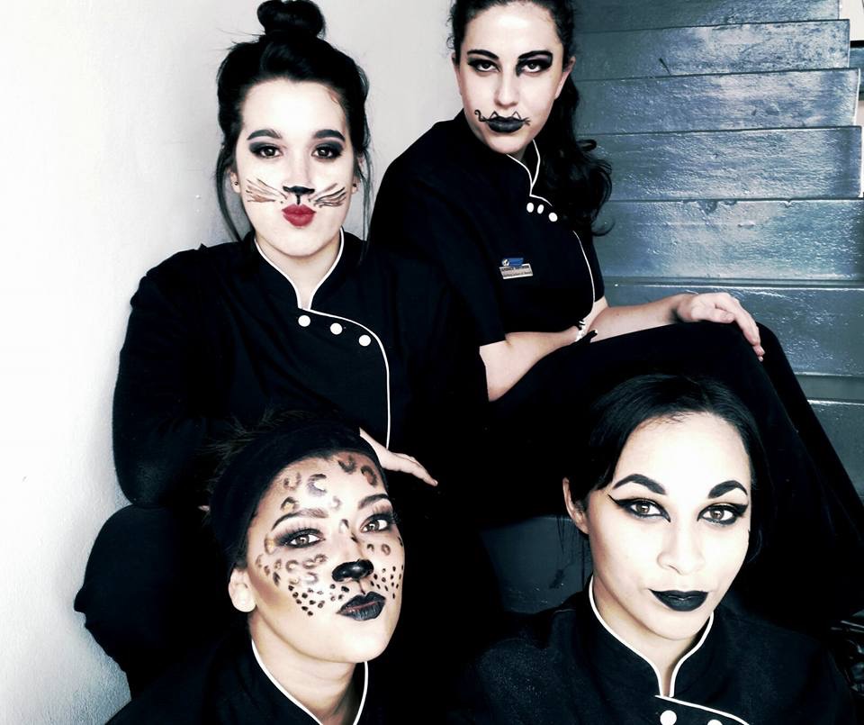 Four beauty students wearing cat-themed makeup and black uniforms