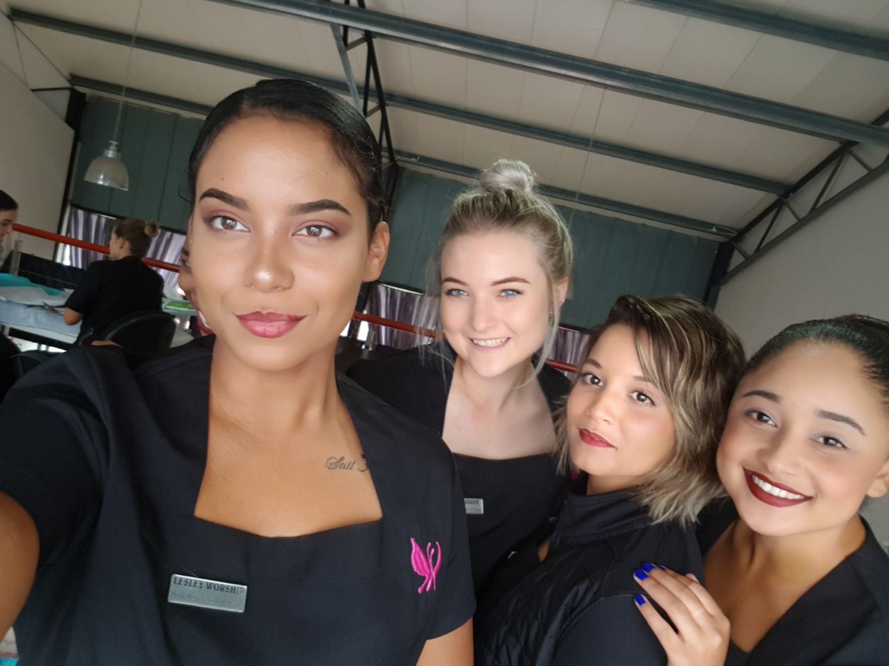 Four smiling women in black uniforms at beauty school